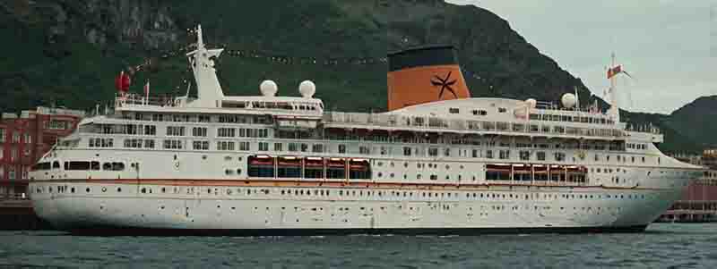 Ein Kreuzfahrtschiff im Hafen mit Bergen im Hintergrund, die eine Küstenlandschaft zeigen.